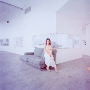 A picture of Utada Hikaru sitting in a greyish living room.