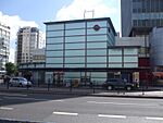 A light blue building with a dark blue sign reading "ELEPHANT & CASTLE STATION" in white letters all under a blue sky with white clouds