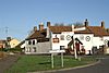 Road junction with direction sign. In the background is a white painted building with a pub sign saying The Crown.