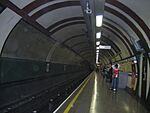 The interior of a building with a rounded ceiling and rounded walls with a railway track on the left and people standing on the right