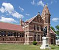 A large stone library building, made of brown and white stone. Windows of the library are separated by small stone columns, and arches of alternating light and dark stone surmount some of the larger windows. The roof line and three-story Gothic tower have decorative stone elements. In front of the building stands a bronze statue of Count Rumford wearing robes.