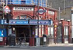 A red-bricked building with a rectangular, white sign reading "ENTRANCE" in black letters and a rectangular, blue sign reading "MAIDA VALE STATION"