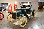 A green-colored, old-fashioned car with two seats and brass fittings