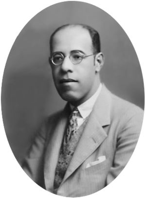 Photograph showing the head and shoulders of de Andrade with glasses wearing a suit