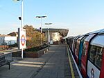 People walking on a railway platform with a train on the right with white siding and red doors all under a blue sky with white clouds