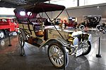 A white-colored, old-fashioned car with four seats and brass fittings