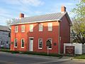 Small rectangular red brick house with white roof and many windows