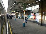 A railway platform with various people walking in different directions on it and a black sign reading "Way out" in yellow letters