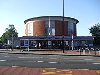 A circular red brick building with concrete roof and glazed screens rises over a lower building