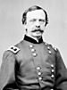 Head and torso of a white man with a pointed mustache and bags under his eyes, wearing a double-breasted military jacket with a rectangular patch over each shoulder.