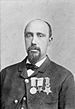 Head and shoulders of a balding black man with a goatee, wearing a suit coat, vest, and bow tie. On the jacket's left breast is a row of three medals.