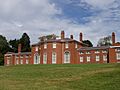 A large brick mansion. The central rectangle of the house has large windows with rounded tops. Wings nearly the width of the central structure extend to either side.