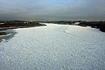 The surface of a wide river approaching a city is almost completely frozen.