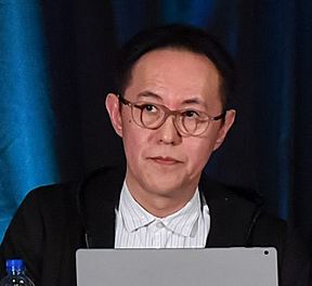 A middle-aged Japanese man with glasses, a black suit, and a red tie.