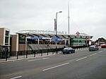 A terracotta-coloured building with a rectangular, light blue sign reading "WEMBLEY PARK STATION" in white letters all under a cloudy sky