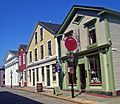 A row of early 19th century buildings line a cobblestoned street. An old-fashioned street lamp is also visible.