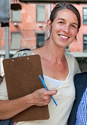 Anne Saxelby holding a pen and a clipboard, smiling and facing the camera.