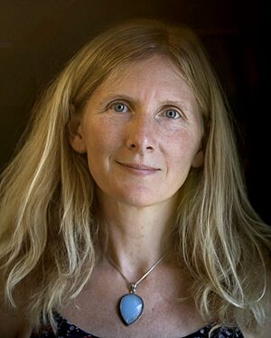 Portrait of Samantha Harvey, a middle-aged woman with blonde hair and light-coloured eyes, wearing a blue necklace and sundress.