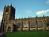 The south front of a church, with a porch and a tower to the left. The tower and the body of the church have pinnacles and crenellations