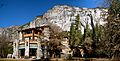 Photograph of The Ahwahnee in winter snow, amidst bare trees with the dramatic walls of Yosemite Valley rising behind.