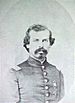 Head and shoulders of a white man with a Van Dyke mustache and curly hair, wearing a military jacket with a star-shaped medal pinned to the left breast.