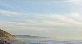 Finger of a mountain visible behind a cliff and on a beach with a partly cloudy sky