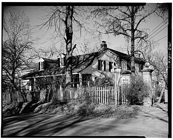 Exterior view of Casa Alvarez, showing several trees, white clapboard siding, front porch, wooden fence, and front two dormer windows