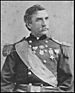 Head and torso of a white man with a mustache and wavy hair wearing an ornate military jacket. The jacket has fringed shoulder boards, a wide sash across the chest, and four medals pinned to the center and left half of the chest.