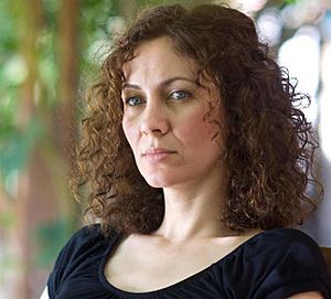 Head shot of Maha Haj, she has shoulder-length curly brown hair. The background is blurry trees