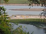 Canoes and tents rest on a sandy spit along a river.