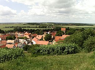 Low hills, barely higher than the church's steeple, surround a village.