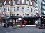 A brown-bricked building with a rectangular, dark blue sign reading "WARREN STREET STATION" in white letters and people in front