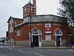 A red-bricked building with a rectangular, blue sign reading "HARROW & WEALDSTONE" in white letters all under a blue sky with white clouds