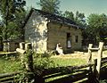 Log cabin in the shadows of trees with a split-rail fence in the foreground