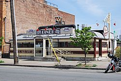 A single-story building in the shape of a railroad car, with an Art Deco facade in cream and maroon stripes situated next to a taller brick building