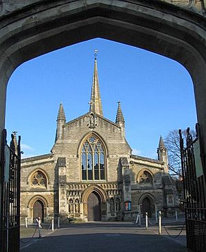 View through an archway of end of a church with a central door flanked by canopied niches containing statues. Arched window above the door and spire behind