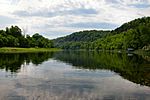 A wide placid river flows by a low wooded hill.