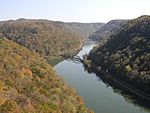 A view of a river winding through a narrow valley, flanked by forested mountain ridges.