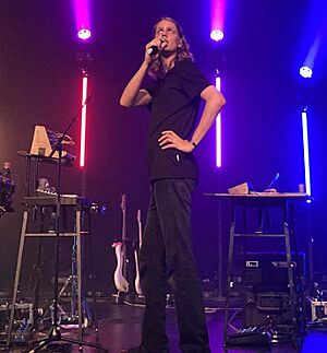 Daði Freyr wearing black pants and t-shirt, standing onstage, appearing to sing or speak into a microphone while looking up