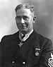 Head and shoulders of a white man with short bristly hair wearing a dark jacket with one round medal pinned to the left breast and a star-shaped medal hanging from a ribbon around his neck.