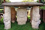 Several stone figures carrying a large flat stone on their heads.