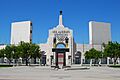 Photograph of the peristyle gate of the Los Angeles Memorial Coliseum, tile mosaicon the underside of the arch, and the Olympic torch reaching to the blue sky.