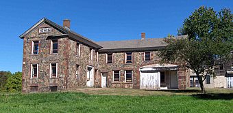 A large L-shaped stone house with missing windows and a tree to the right