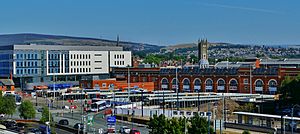 A Metrolink and bus station in front of office buildings. There are hills in the background and a road in the foreground