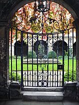 A view looking through a wrought-iron gate to a patch of grass with stone arches beyond.