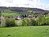 The roofs of houses and farm buildings in a green valley. Trees in the foreground