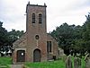 A small brick-built church with the tower in the centre. To the right are gravestones and in the background are trees