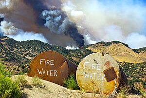 Two tanks marked Fire Water sit in readiness to be used, as a California brush fire burns in the background, 2010