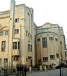 A cylindrical drum-shaped stair structure in cream stone sits at the junction of two taller blocks