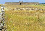 Grass field, stone enclosures and a fortress in the background